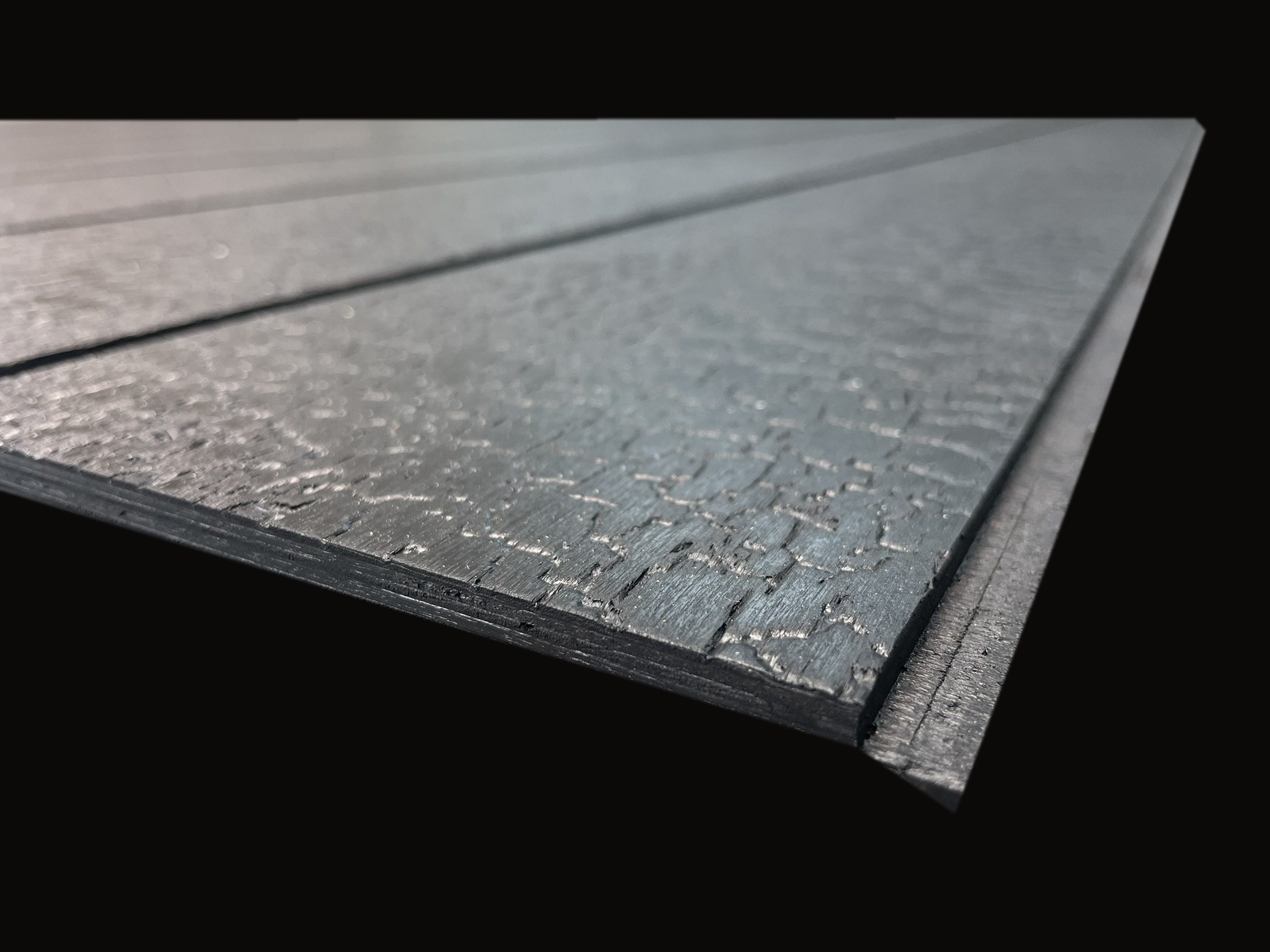 Low-angle view of a Shiplap Scorched panel on black, showing the charred-timber crackle texture and the routed shiplap rebate along the edge
